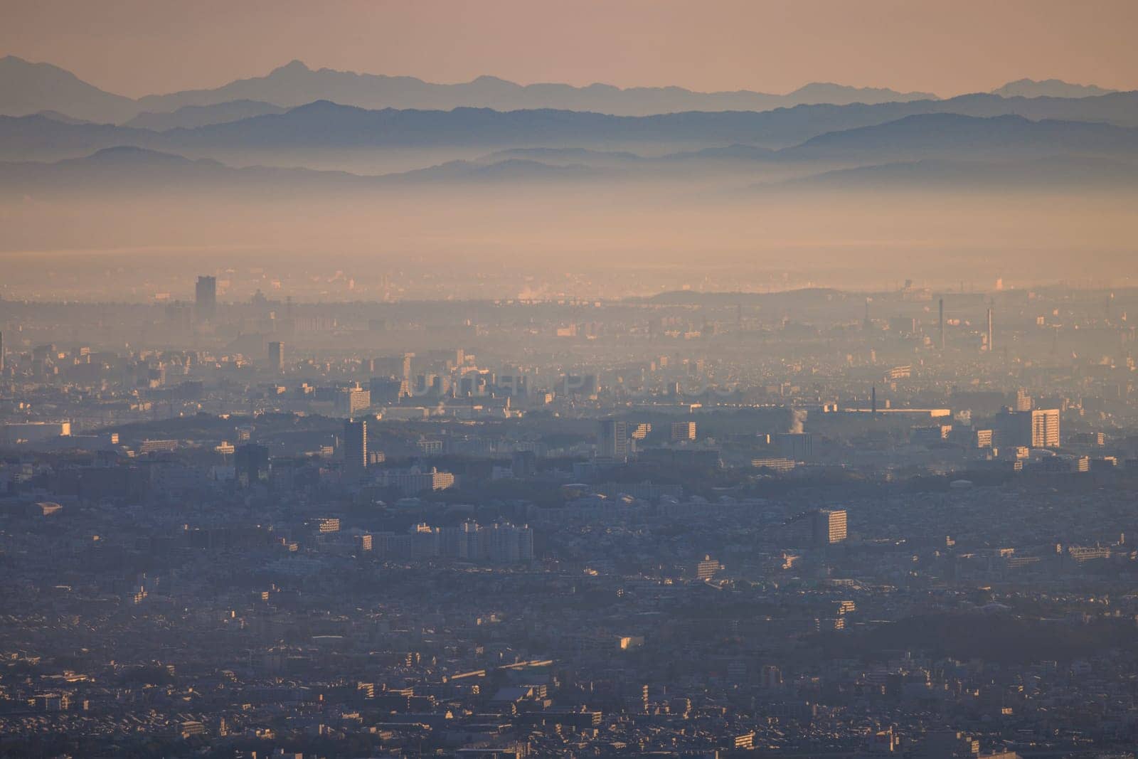 Sprawling city blends with smog layer and distant mountains at sunrise by Osaze