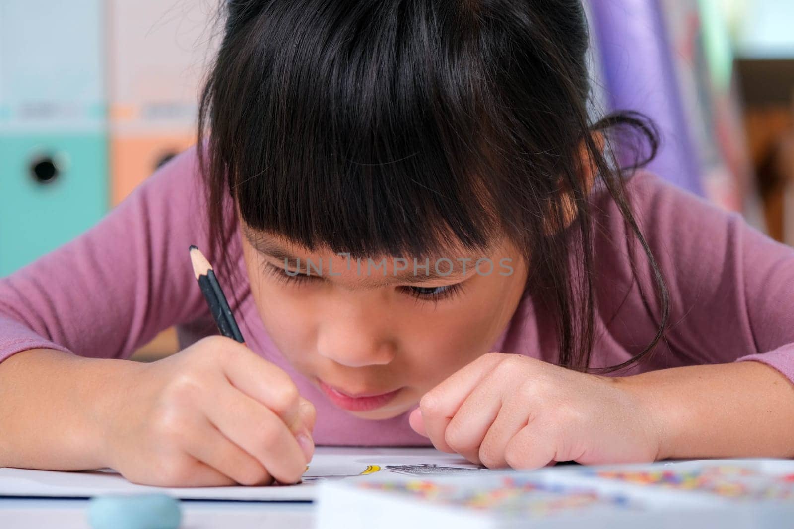Happy little girl drawing with colored pencils on paper sitting at table in her room at home. Creativity and development of fine motor skills. by TEERASAK