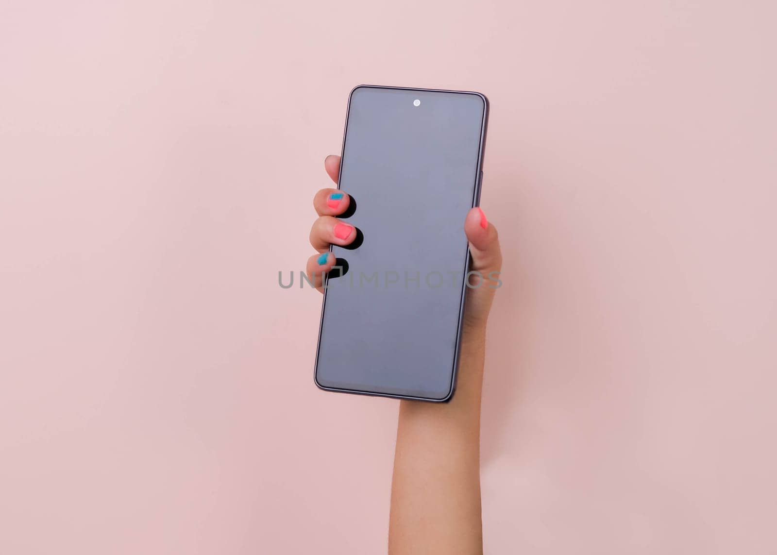 Girl hand holding smartphone on pink background in studio. Mobile phone mockup for your product. by TEERASAK