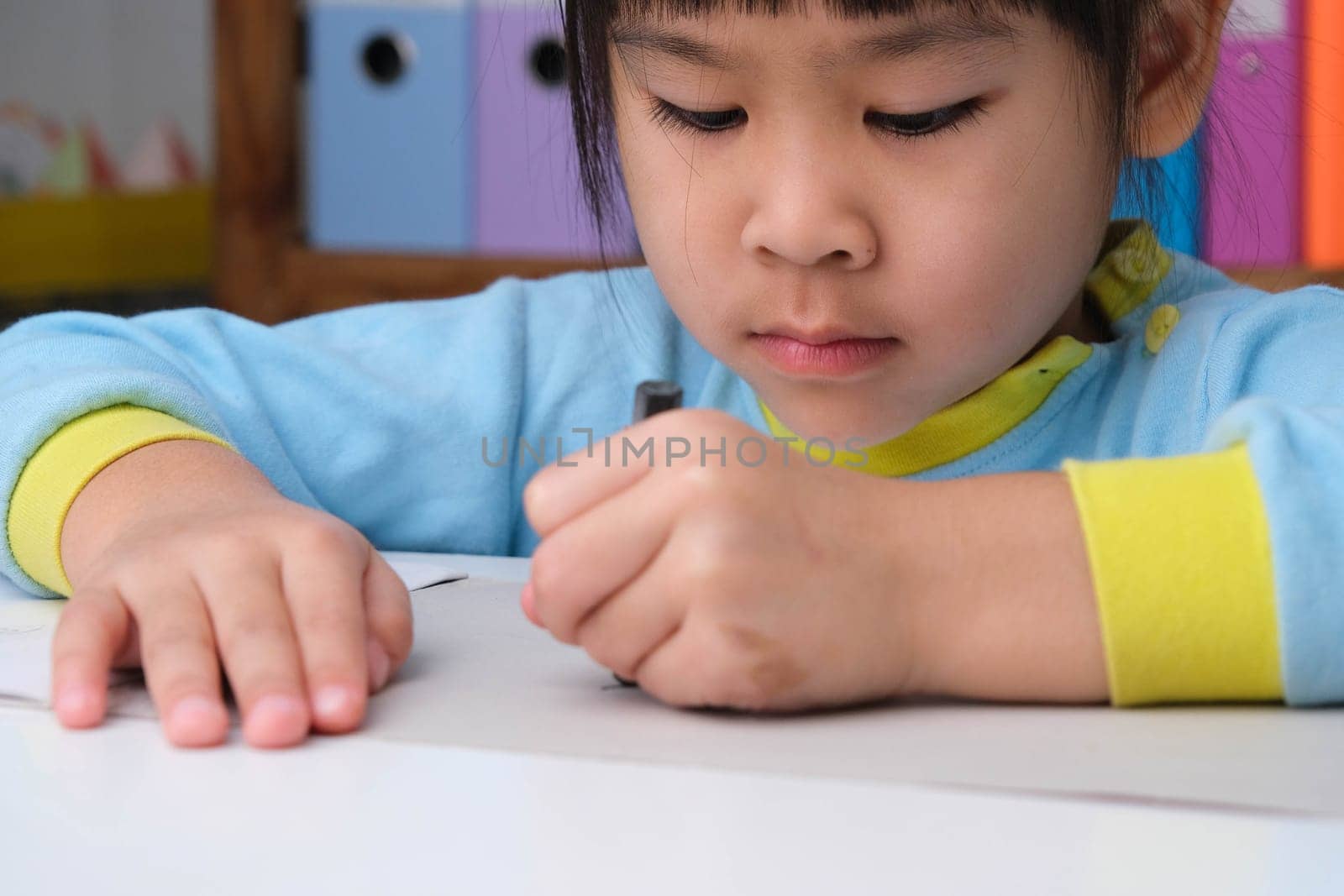 Cheerful happy little girl drawing with crayons on paper sitting at table in her room at home. Creativity and development of fine motor skills. by TEERASAK