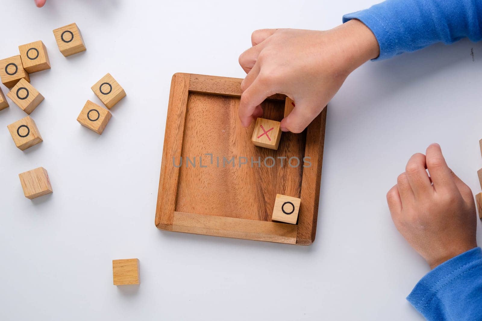 Little siblings playing wooden board game tic-tac-toe on table in living room. Family spending time together on weekend. by TEERASAK