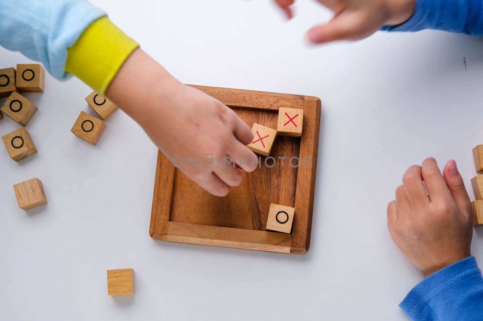 Little siblings playing wooden board game tic-tac-toe on table in living room. Family spending time together on weekend. by TEERASAK