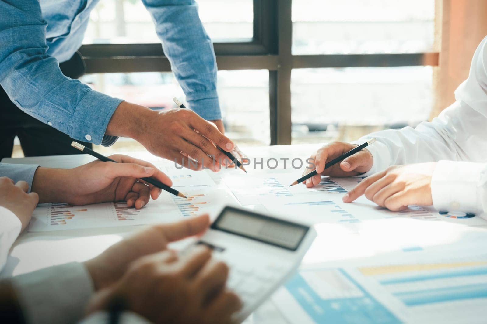 Close-up of businessmen working together at workplace, discussing about strategies, plans, analytic progress, and financial stats, and pointing at graph documents on desk holding pencils and calculator. Business and Teamwork concept.