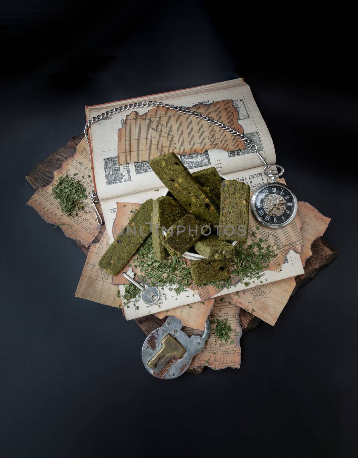 Bangkok, Thailand - Mar 17, 2023 : Homemade Cannabis Snack Sticks in the steel cup are on the Old Song Book with the Analog Pocket Watch and Vintage Iron Padlock on old wooden plank with dark backgroud. The Concept of Relaxation and the Happiness, Vintage style, Space for text. Top view.