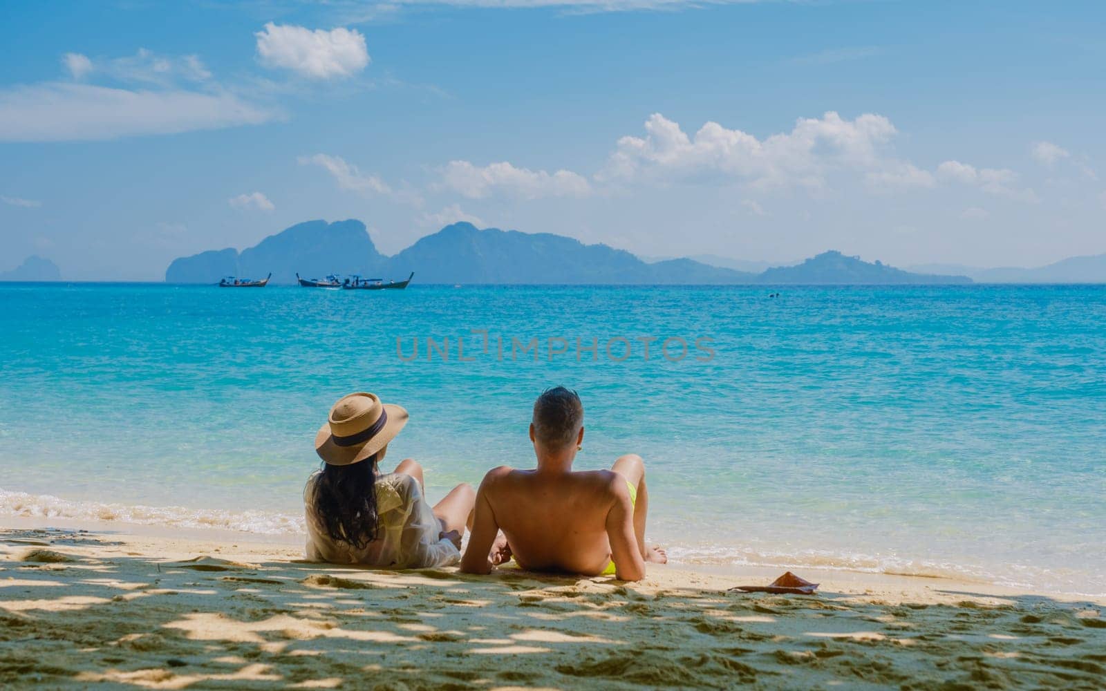 the backside of a couple of men and women sitting at the beach of Koh Kradan island in Thailand by fokkebok
