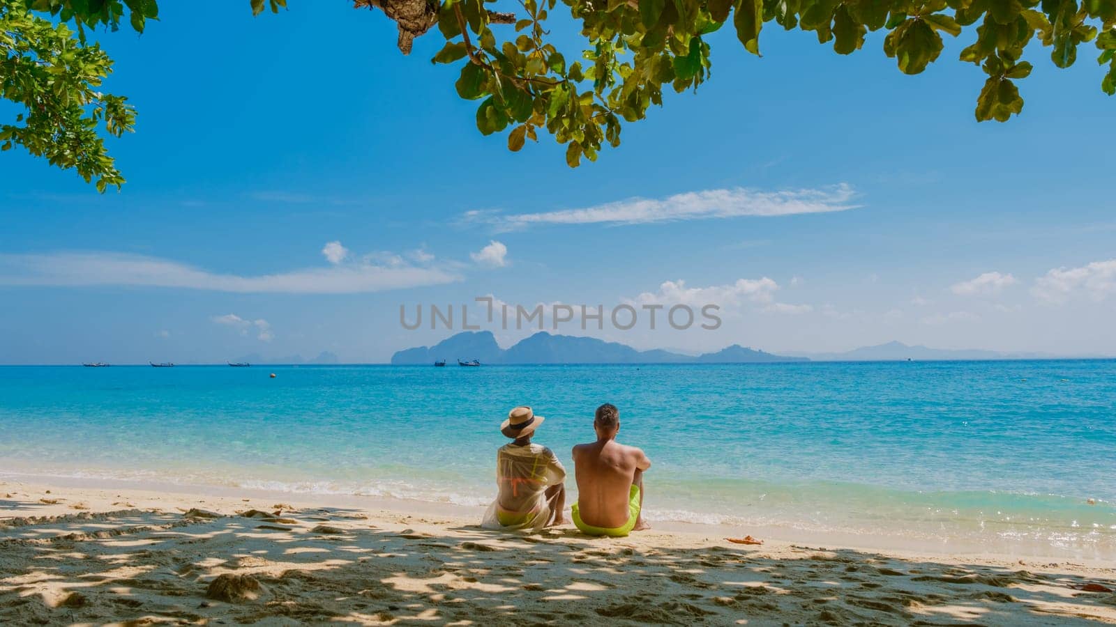 the backside of a couple of men and women sitting at the beach of Koh Kradan island in Thailand by fokkebok