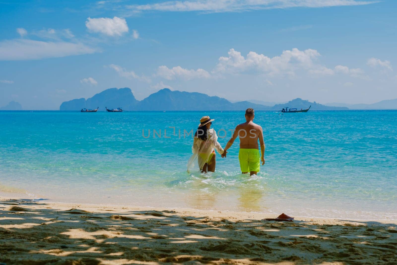 a couple of men and women walking at the beach of Koh Kradan island in Thailand during vacation on a sunny day