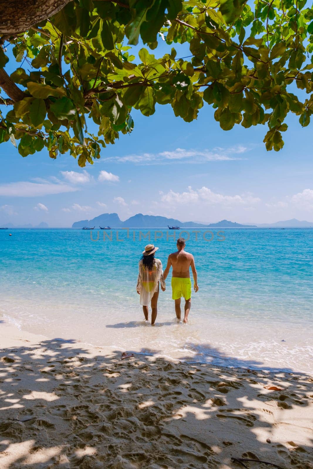 a couple of men and women walking at the beach of Koh Kradan island in Thailand during vacation on a sunny day