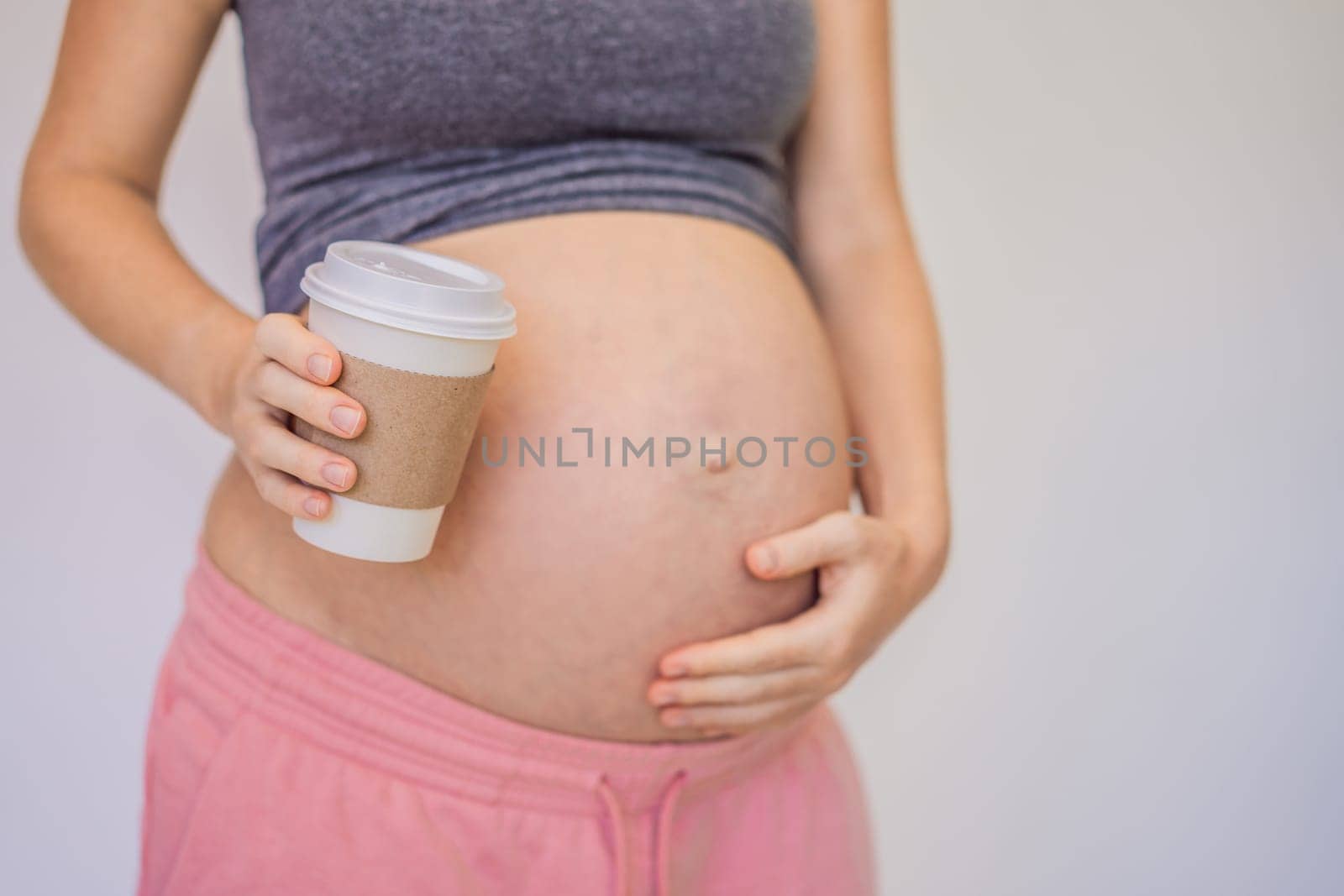 A pregnant woman holds a cup of coffee in her hands. Caffeine safety, myths about coffee during pregnancy concept.