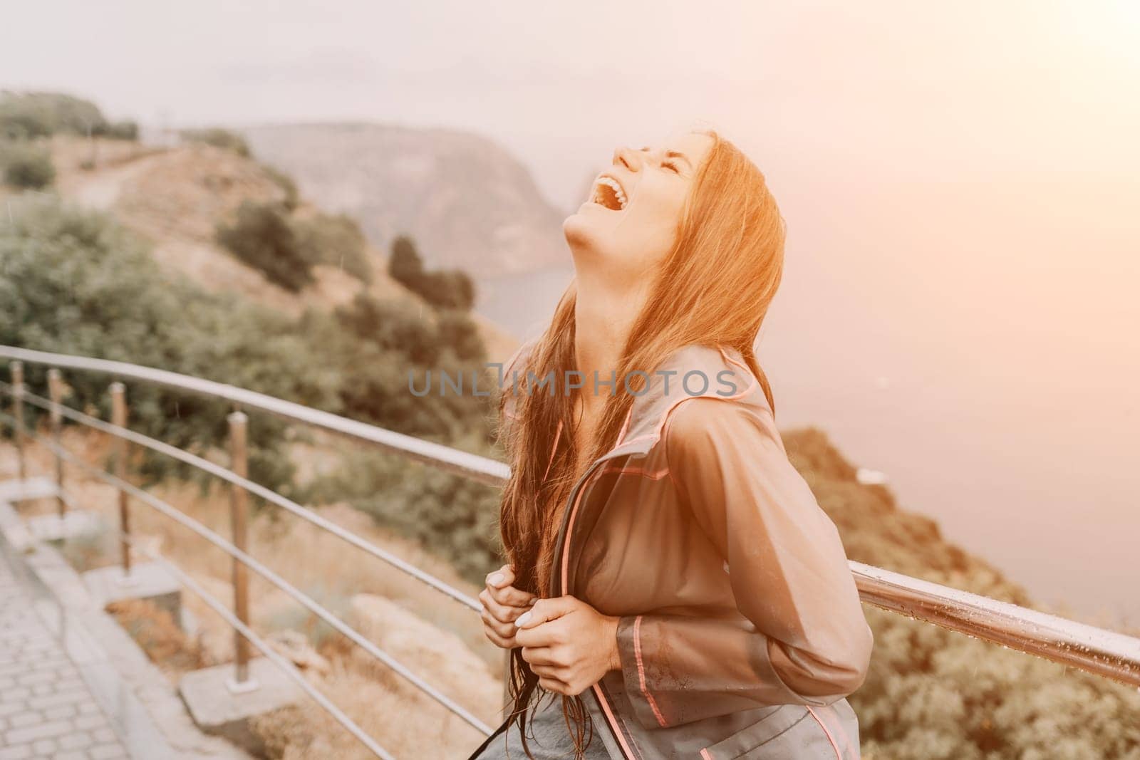 Woman rain umbrella. Happy woman portrait wearing a raincoat with transparent umbrella outdoors on rainy day in park near sea. Girl on the nature on rainy overcast day. by panophotograph