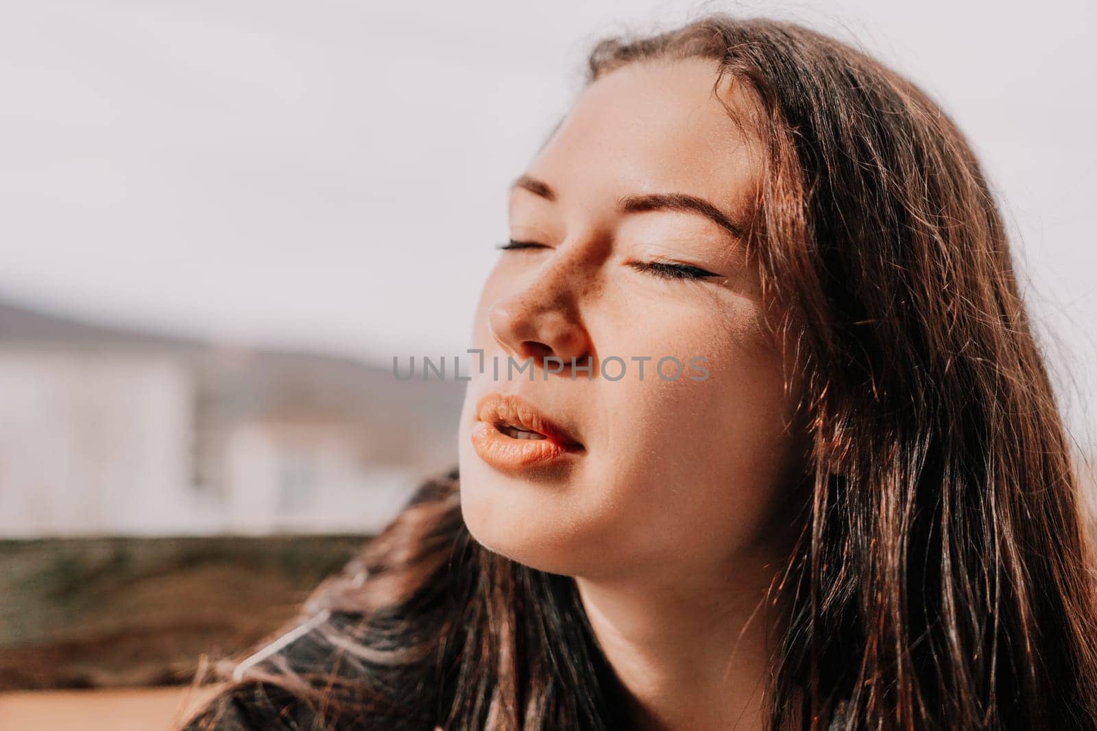 Happy young smiling woman with freckles outdoors portrait. Soft sunny colors. Outdoor close-up portrait of a young brunette woman and looking to the camera, posing against nature background.