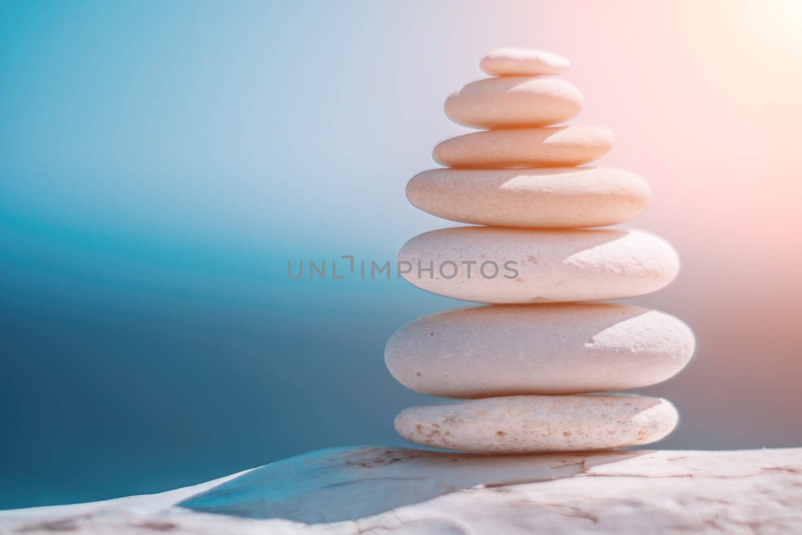 Balanced rock pyramid on sea pebbles beach, sunny day and clear sky at sunset. Golden sea bokeh on background. Selective focus, zen stones on sea beach, meditation, spa, harmony, calm, balance concept by panophotograph