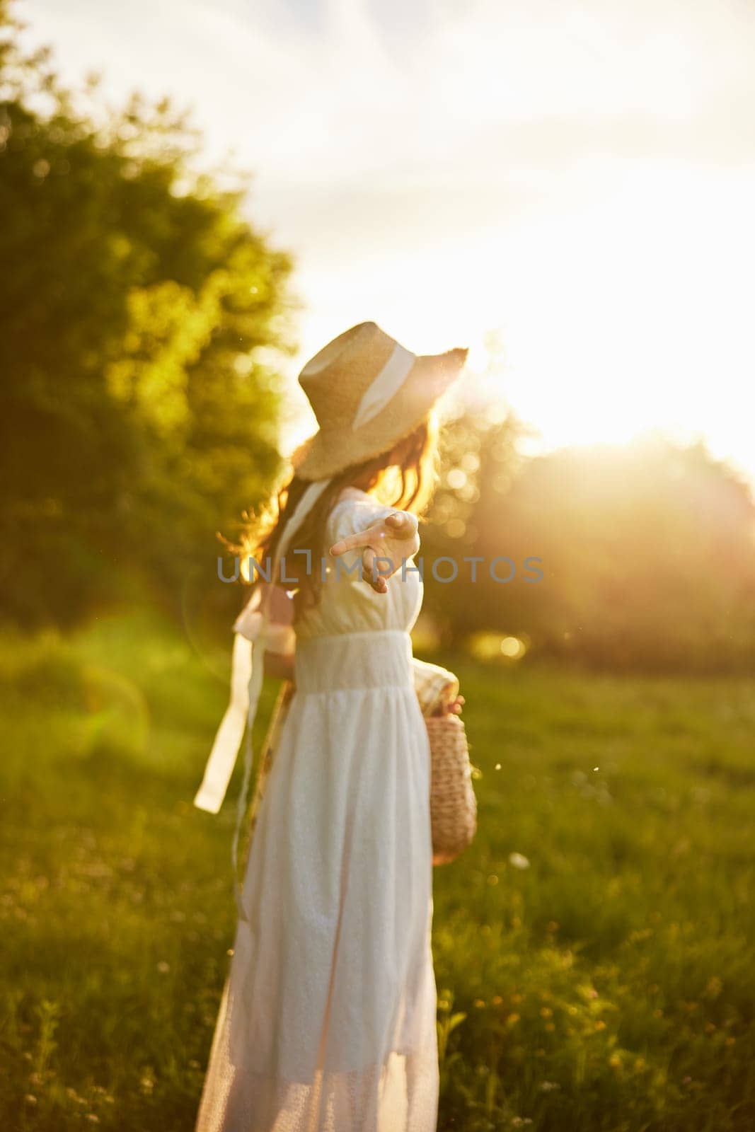 A woman in a light dress stands in the countryside with her back to the camera and holds out her hand. High quality photo