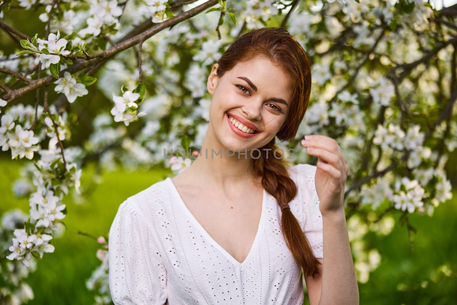 a joyful, carefree woman in a light dress stands against the background of a flowering tree by Vichizh