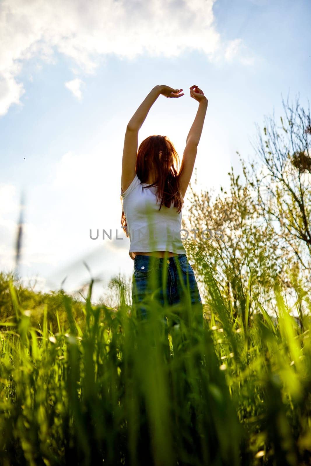 joyful slender woman posing in a field with her arms raised high by Vichizh