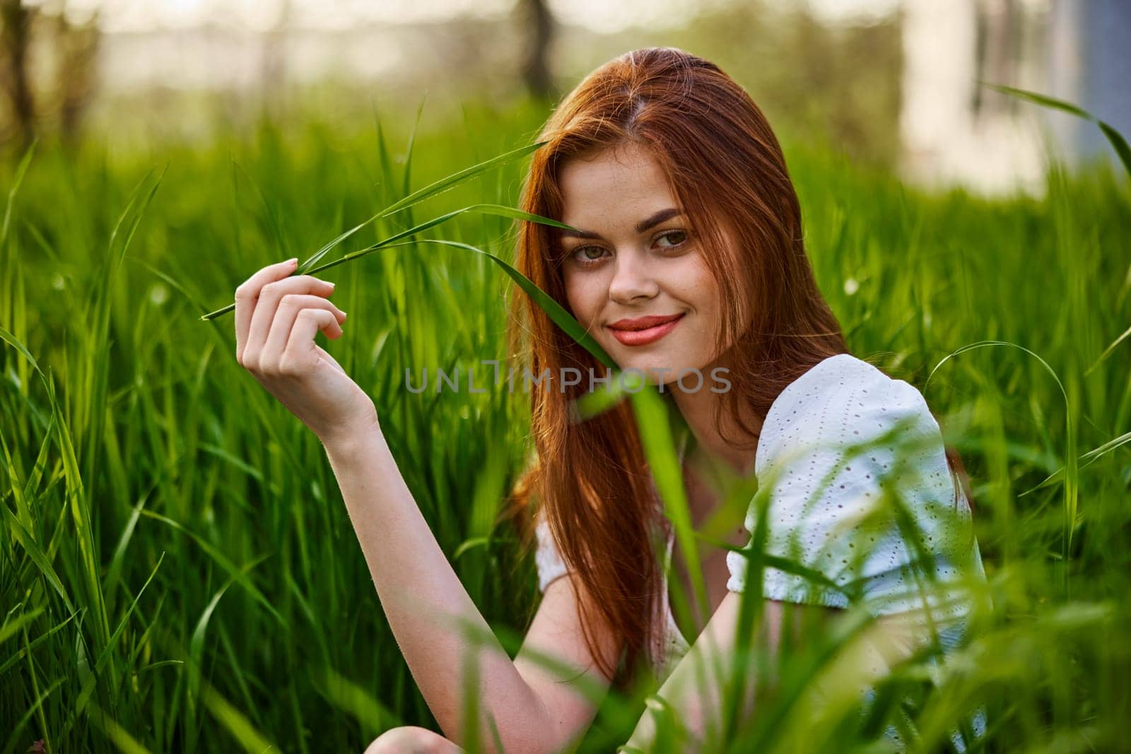 portrait of a cute red-haired woman sitting in tall grass and holding a leaf in her hands. High quality photo