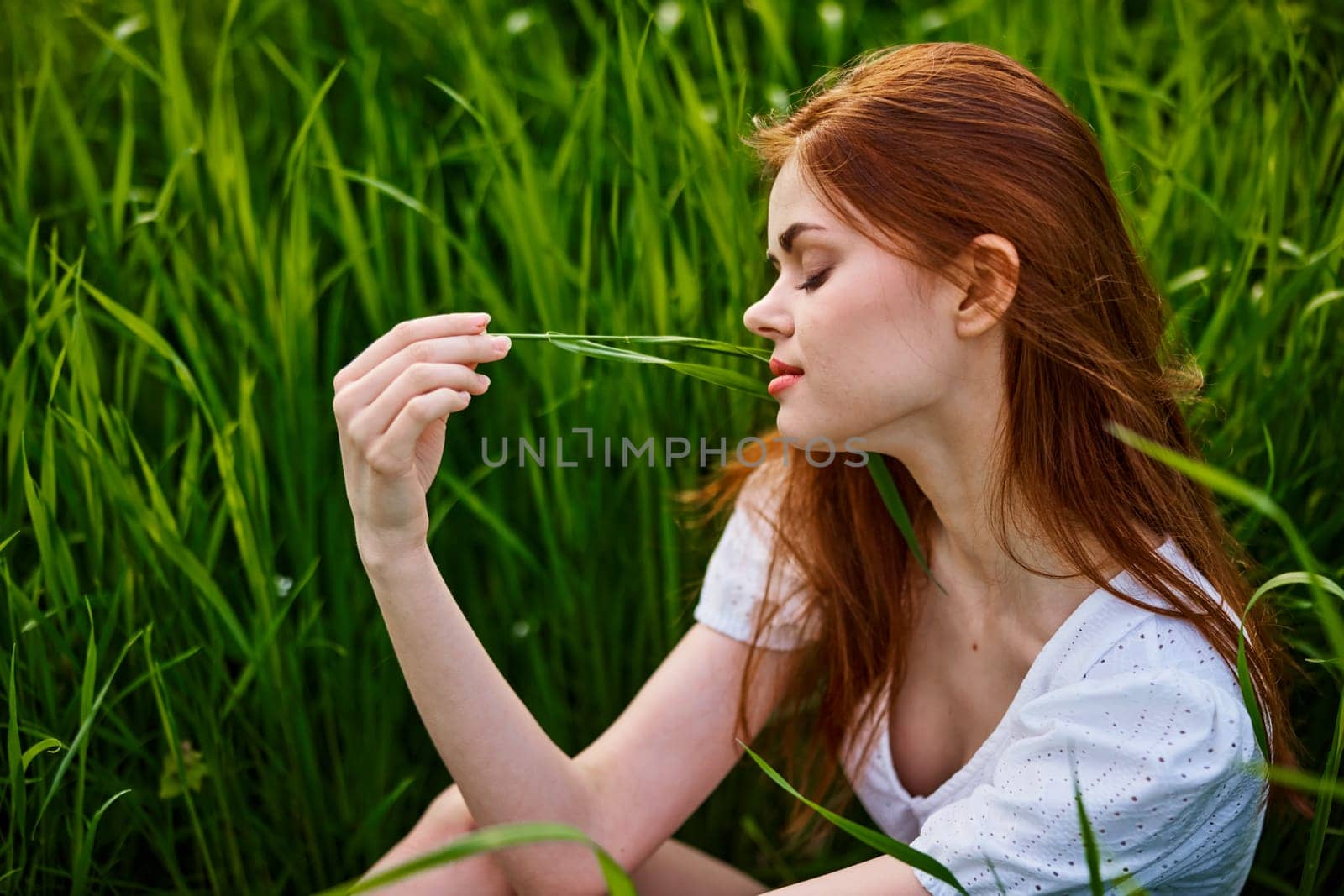 portrait of a beautiful redhead woman sitting in the grass on a sunny day at sunset. High quality photo