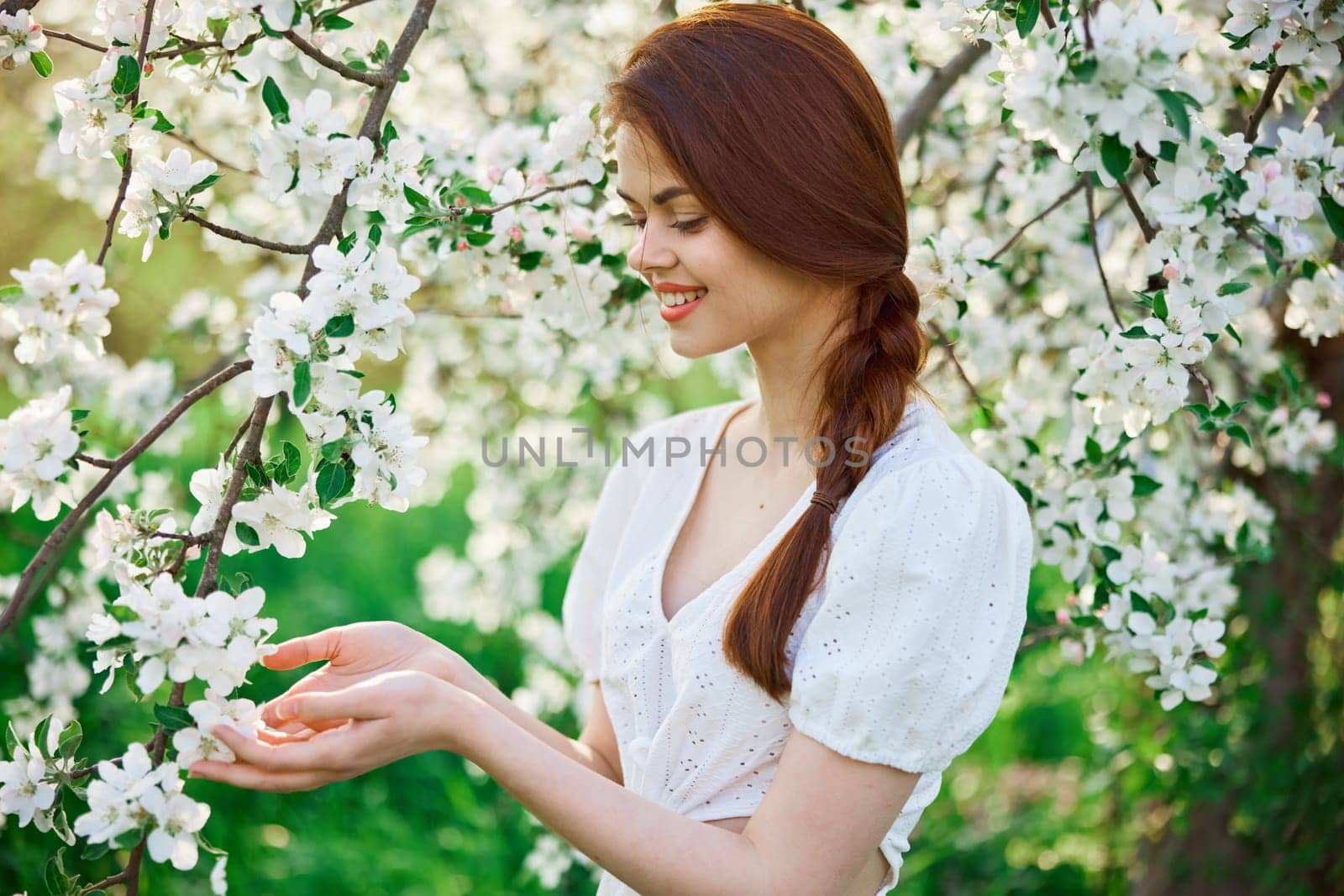 a beautiful woman in a light dress enjoys the spring while standing next to a flowering tree by Vichizh