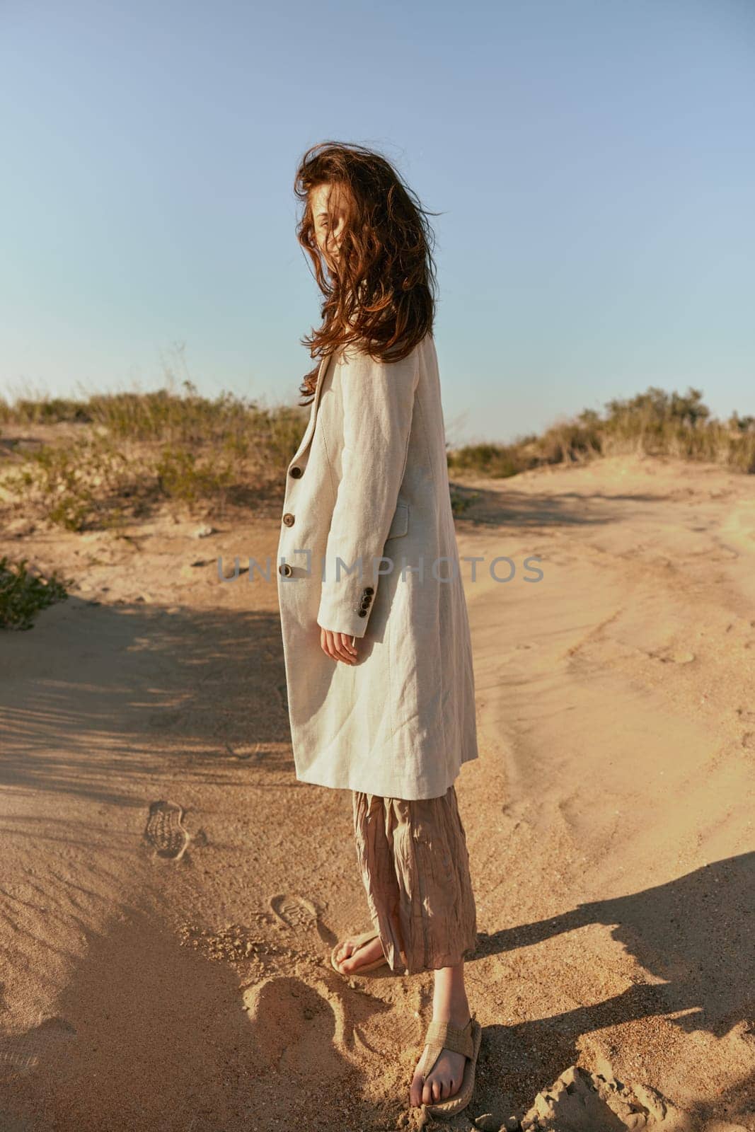 stylishly dressed woman stands posing in the desert in windy weather by Vichizh