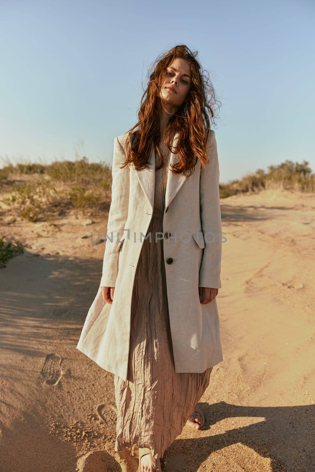 stylishly dressed woman stands posing in the desert in windy weather by Vichizh