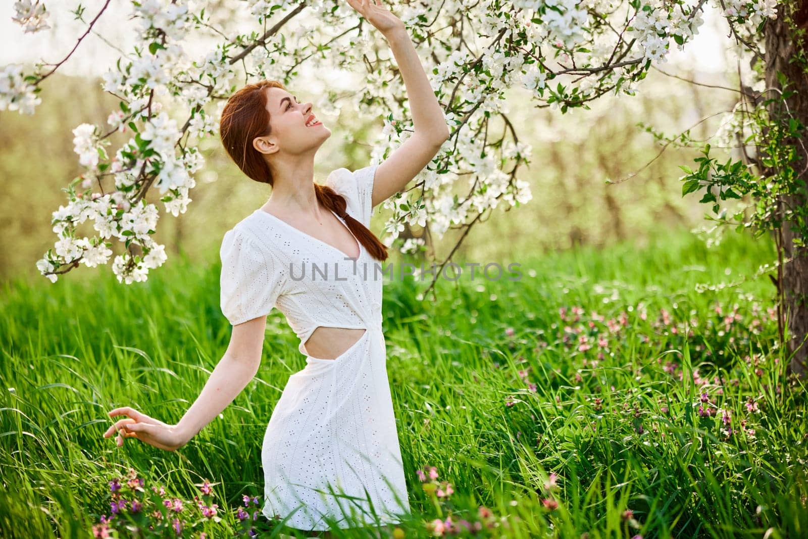 beautiful woman in a light dress posing next to a flowering tree in the countryside by Vichizh