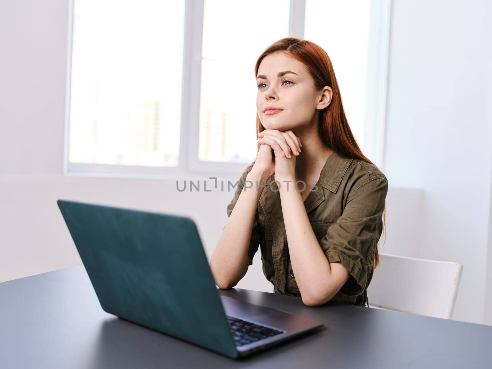 pensive woman sits in the office at the table with a laptop and works by Vichizh