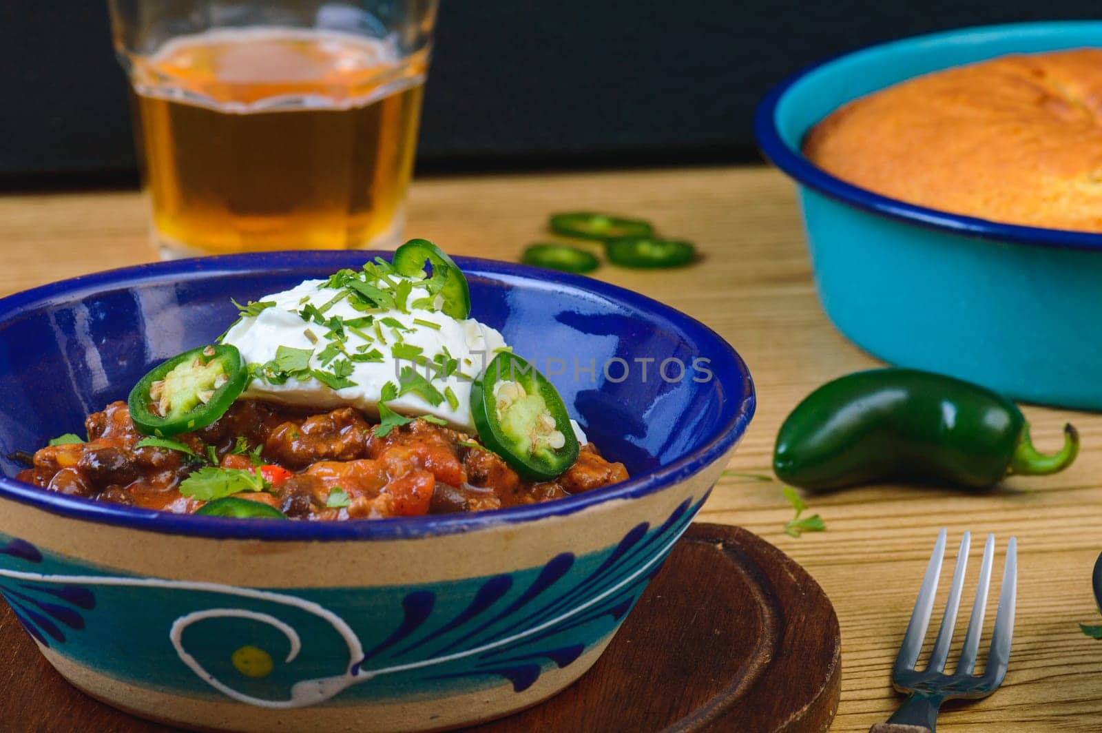 Black bean chili con carne in bowl with corn bread, potatoes. and beer. Tex-Mex style beef chili with sour cream, cilantro and jalapenos.