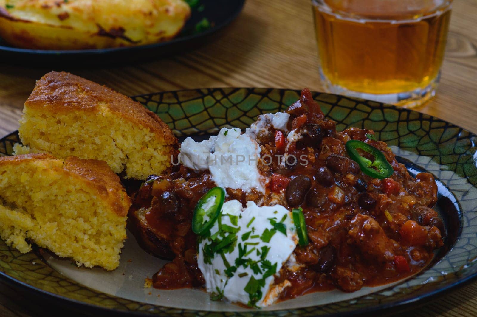 Black bean chili con carne in bowl with corn bread, potatoes. and beer. Tex-Mex style beef chili with sour cream, cilantro and jalapenos.