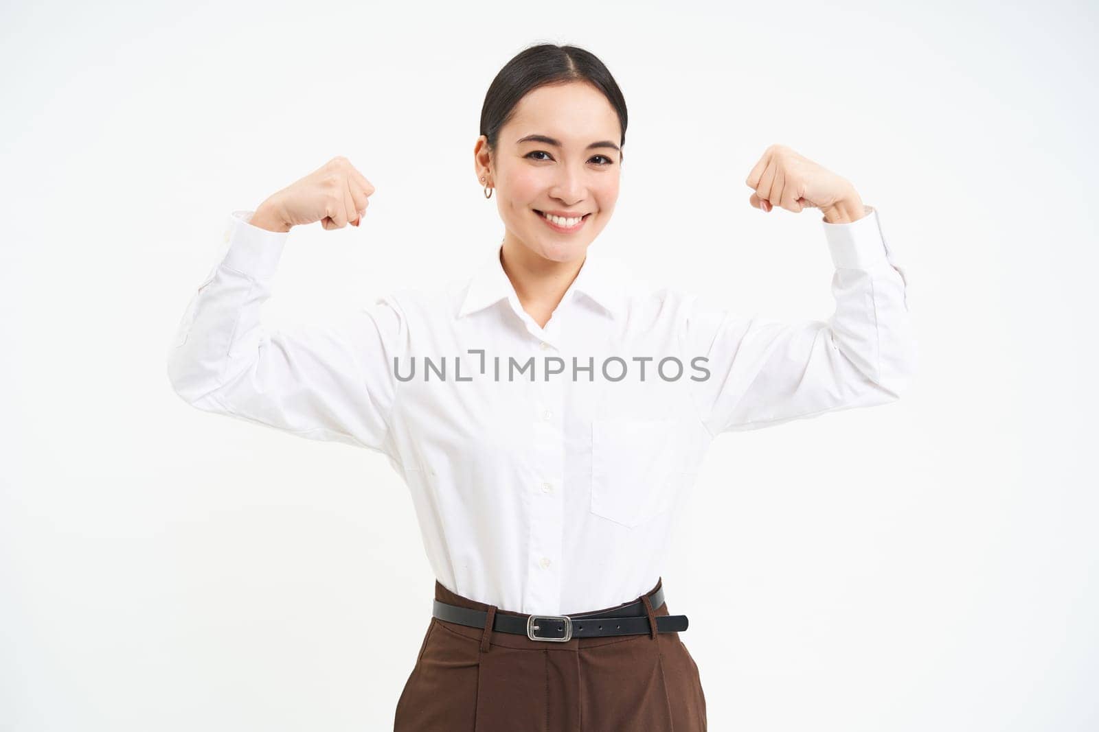Business and corporate women. Strong and successful asian woman entrepreneur, shows biceps, flexing muscles, smiling pleased, white background by Benzoix