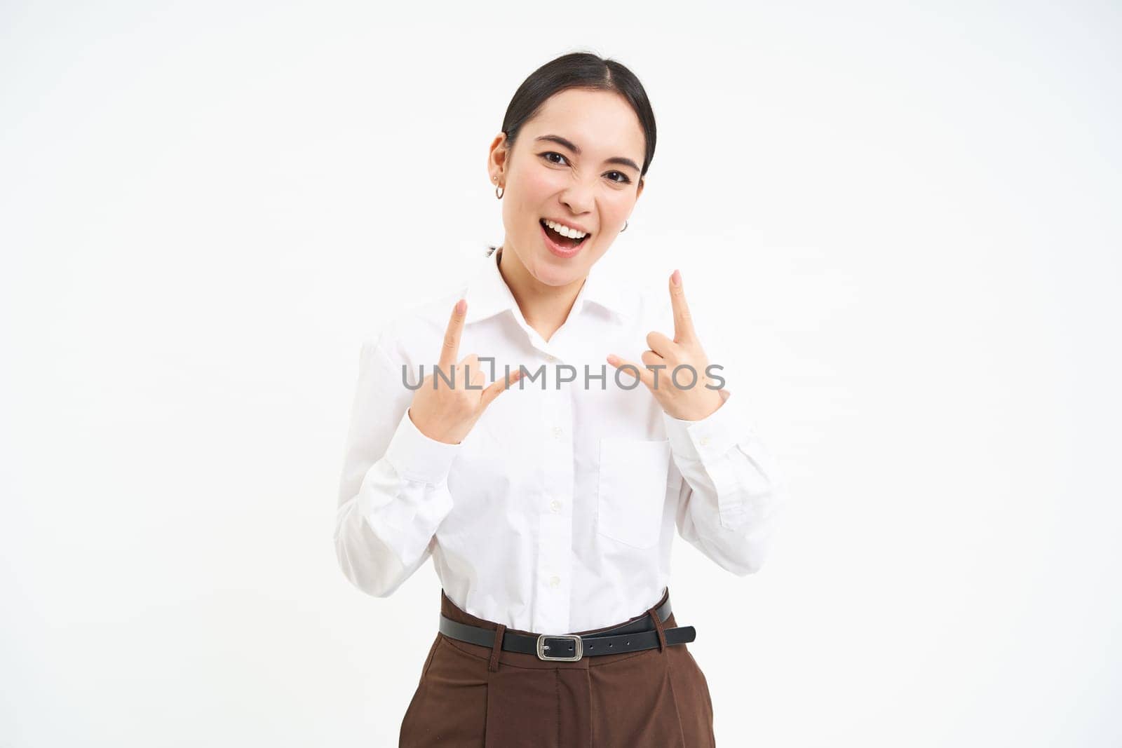 Excited smiling businesswoman, asian female employee, has fun, shows heavy metal, rock n roll gesture, celebrates, white background.