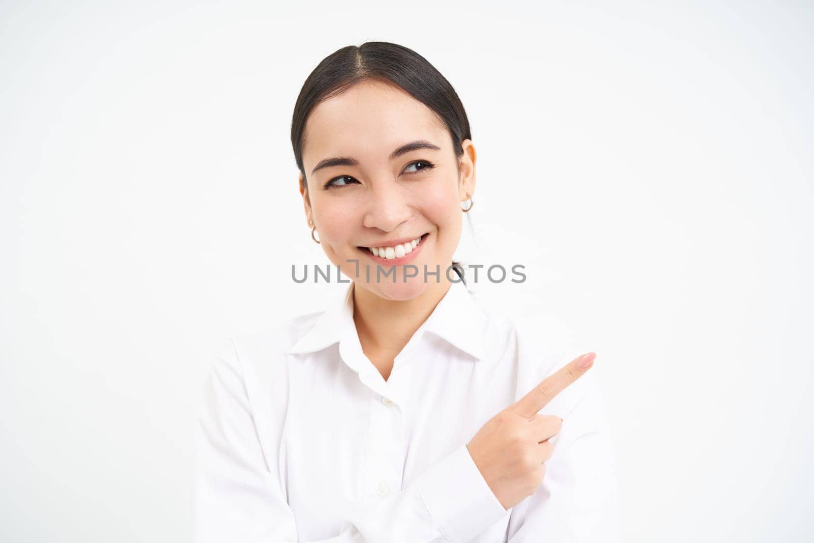 Successful korean businesswoman, pointing finger right, showing advertisement on banner, standing over white background.