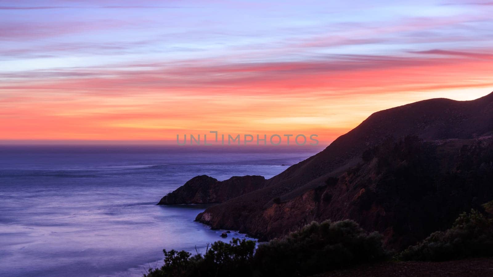 Mountain slopes into Pacific Ocean on rugged coast with beautiful sunset by Osaze