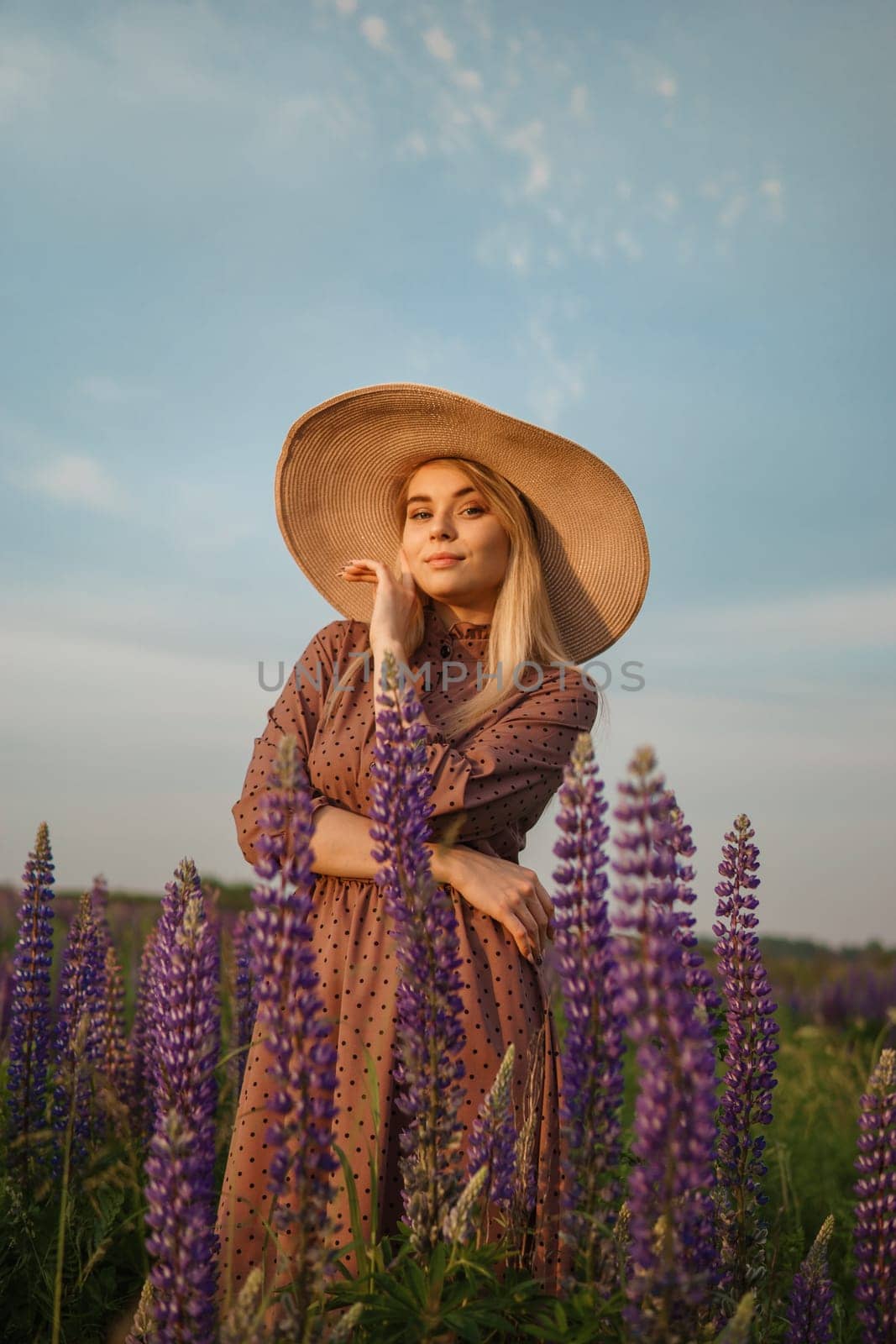 A beautiful woman in a straw hat walks in a field with purple flowers. A walk in nature in the lupin field.