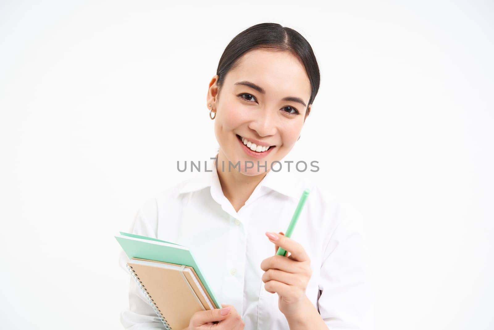 Beautiful confident korean woman, student with pen and notebooks, smiling and looking happy, standing over white background.