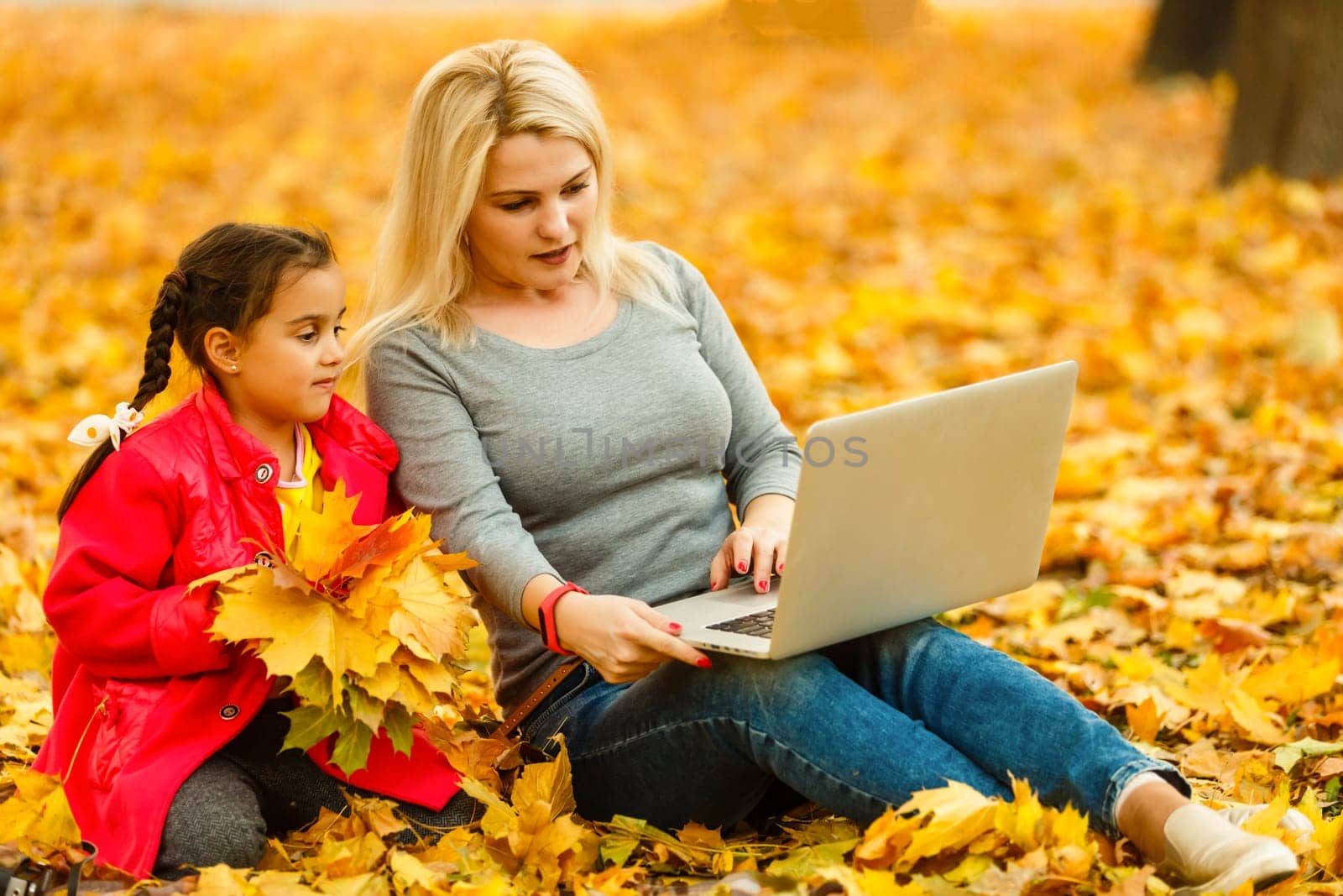 mother and daughter work on laptop outside in autumn. by Andelov13