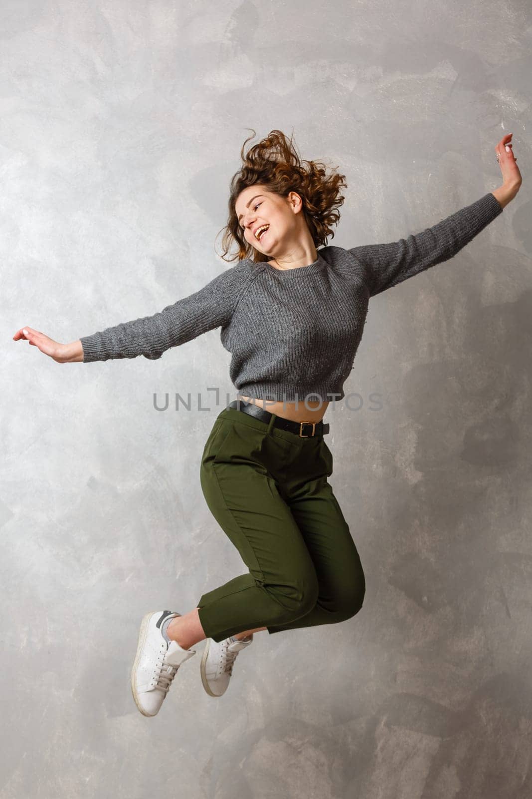 Portrait of cheerful positive girl jumping in the air with raised fists looking at camera isolated.