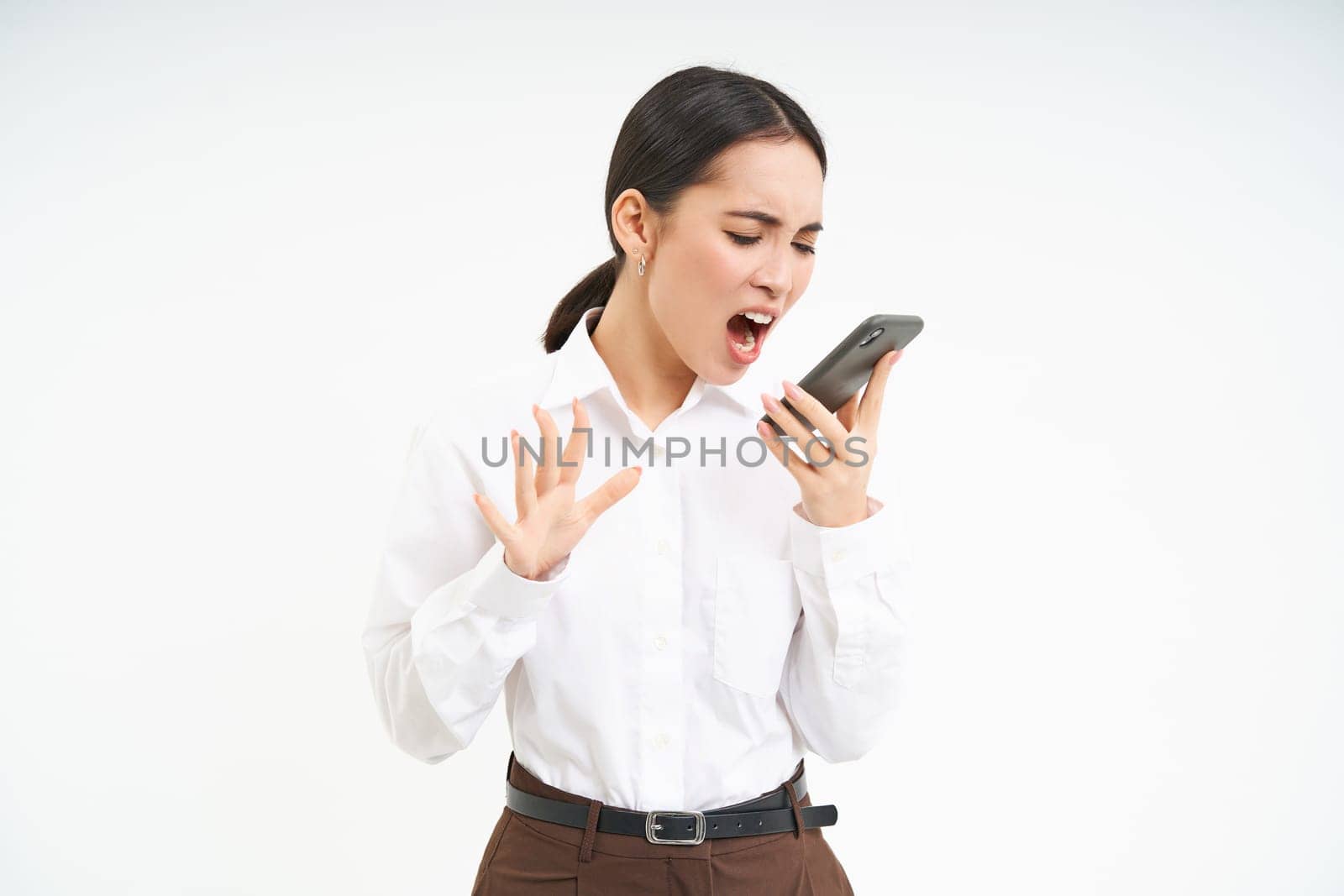 Angry business woman shouts at mobile phone, has intense conversation on telephone, stands over white background by Benzoix