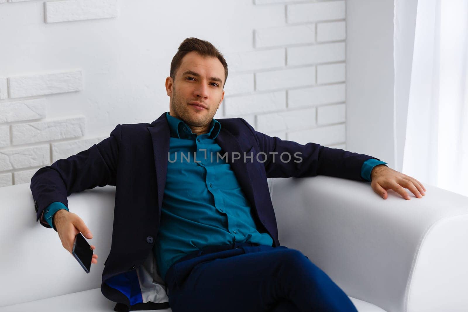 Handsome young man working while sitting on the couch in office by Andelov13