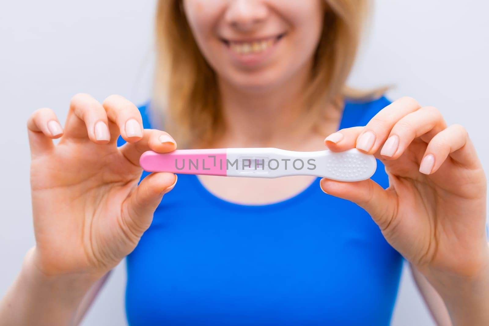 Smiling woman in blue holding a positive pregnancy test.