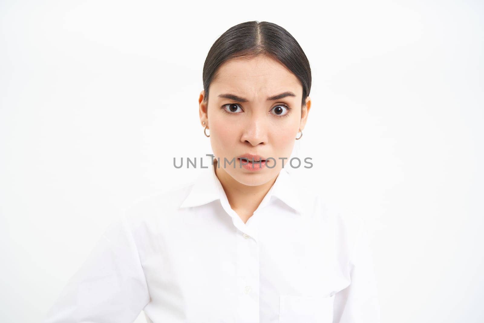 Portrait of asian businesswoman, office lady with shocked face, looks confused at camera, stands over white background.