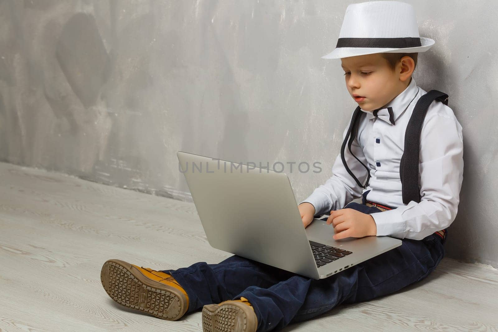 Little boy using laptop against grey wall background by Andelov13