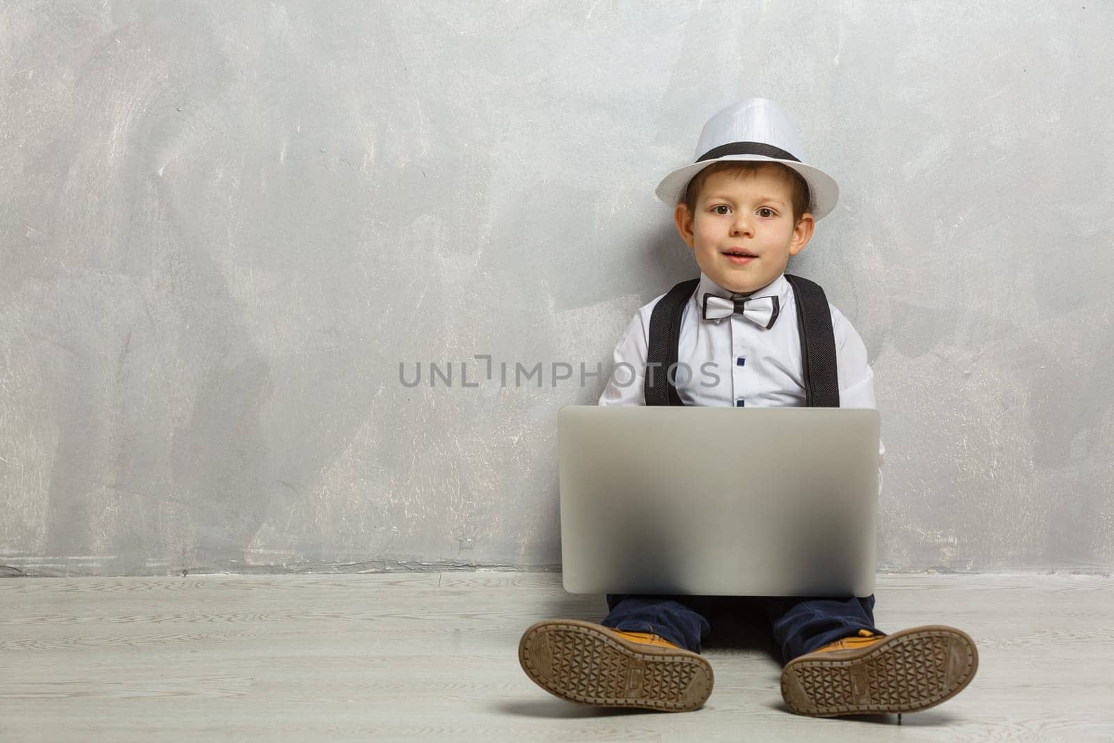 Young man sits on the laminate floor with black laptop.