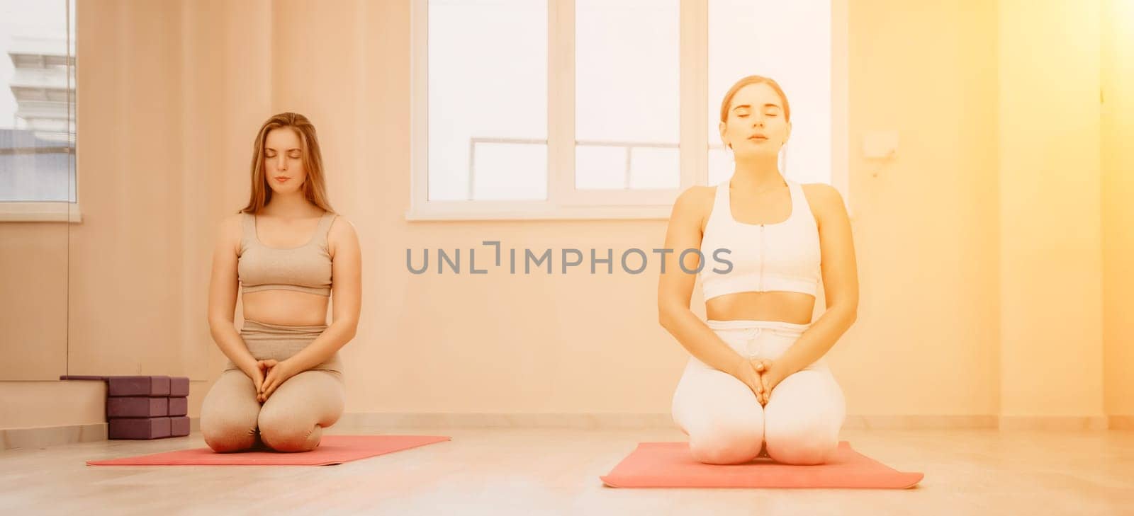 Two young sporty woman, fitness instructor in sportswear doing stretching and pilates on yoga mat in the studio with mirror. Female fitness yoga routine concept. Healthy lifestyle and harmony. by panophotograph