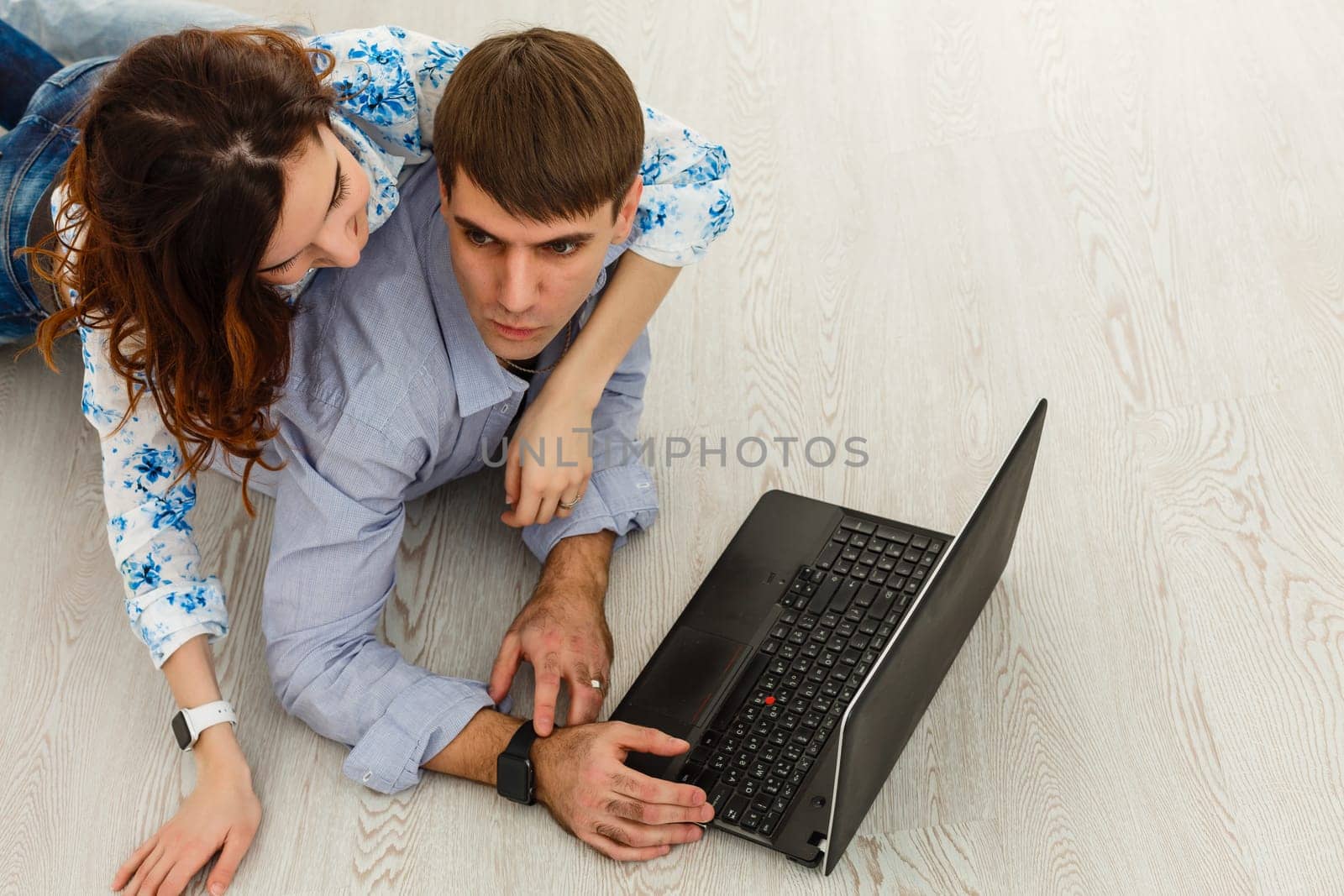 Couple Use Laptop Computer, while Sitting on the Living Floor room of their Apartment. Boyfriend and Girlfriend Talk, Shop on Internet, Choose Product to Order Online, Watch Streaming Service