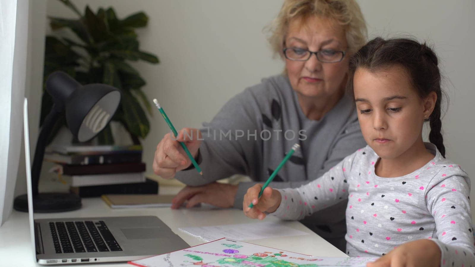 little girl studying with her grandmother at home, use laptop for education, online study, home studying. Girl has homework at distance learning. Lifestyle concept for Family quarantine covid-19.