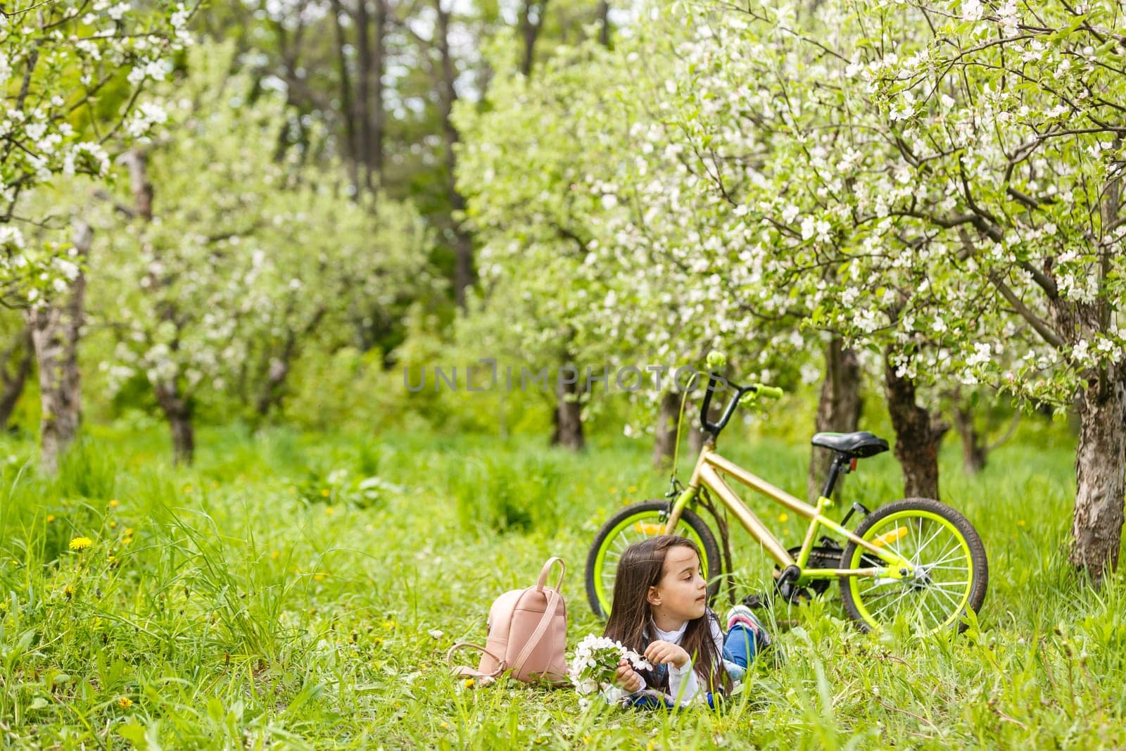 a little girl lies on the grass near the blossoms.