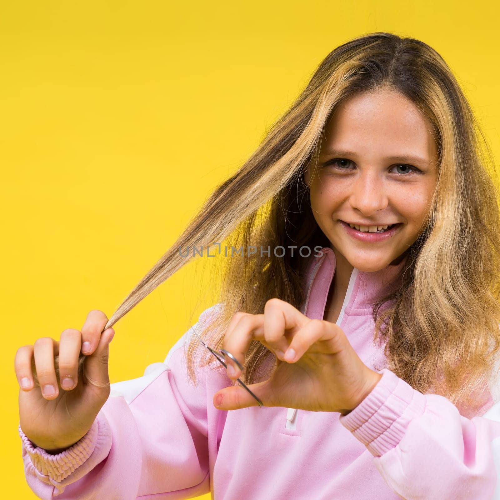 Child adorable girl hairdresser cutting long blonde hair with metallic scissors on yellow by Zelenin