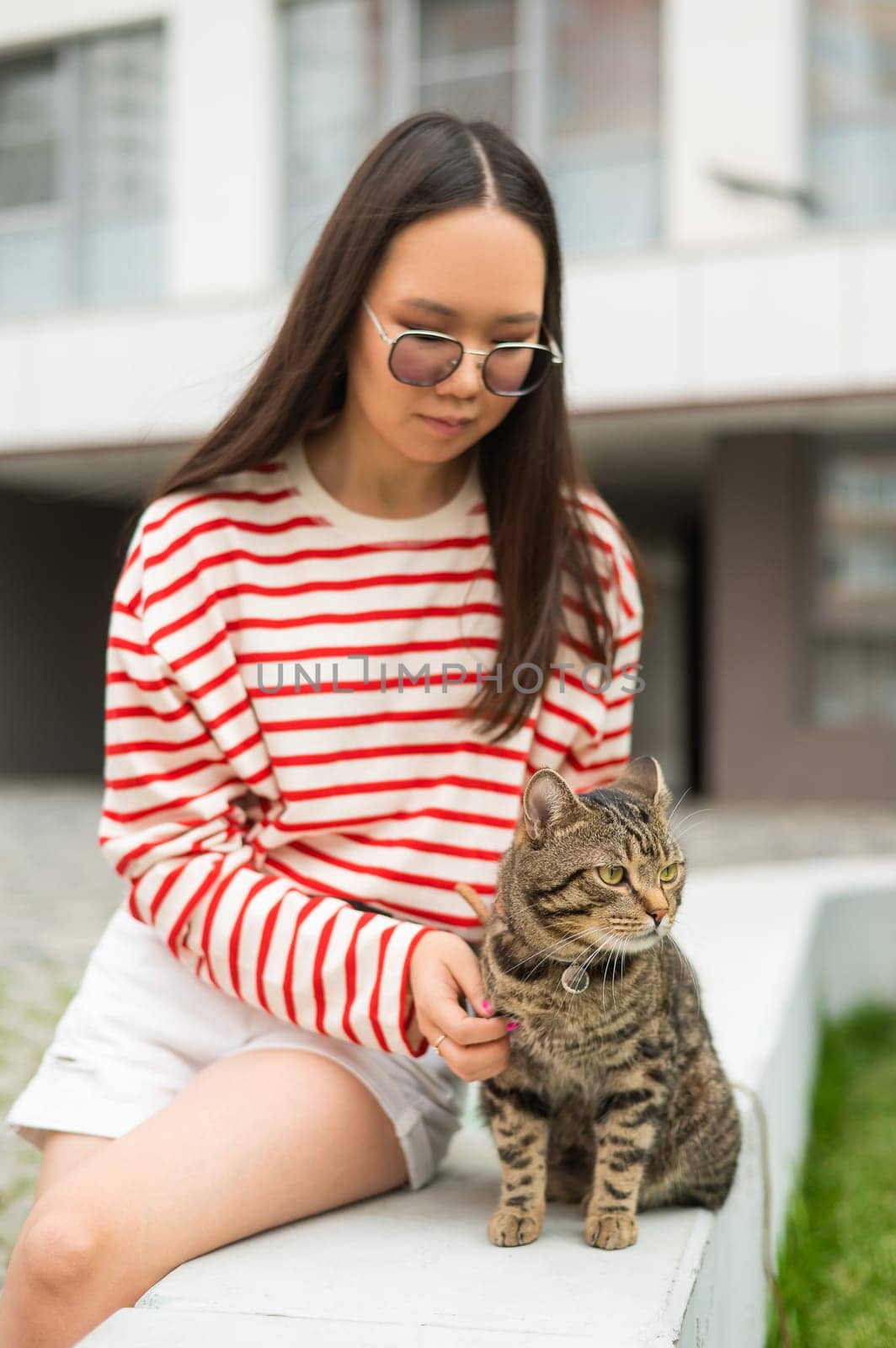 Young woman and tabby cat sitting on a bench outdoors