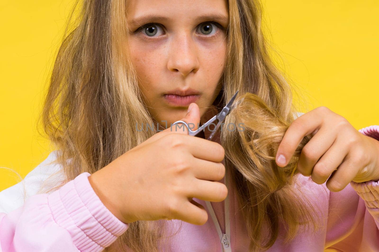 Child adorable girl hairdresser cutting long blonde hair with metallic scissors on yellow by Zelenin