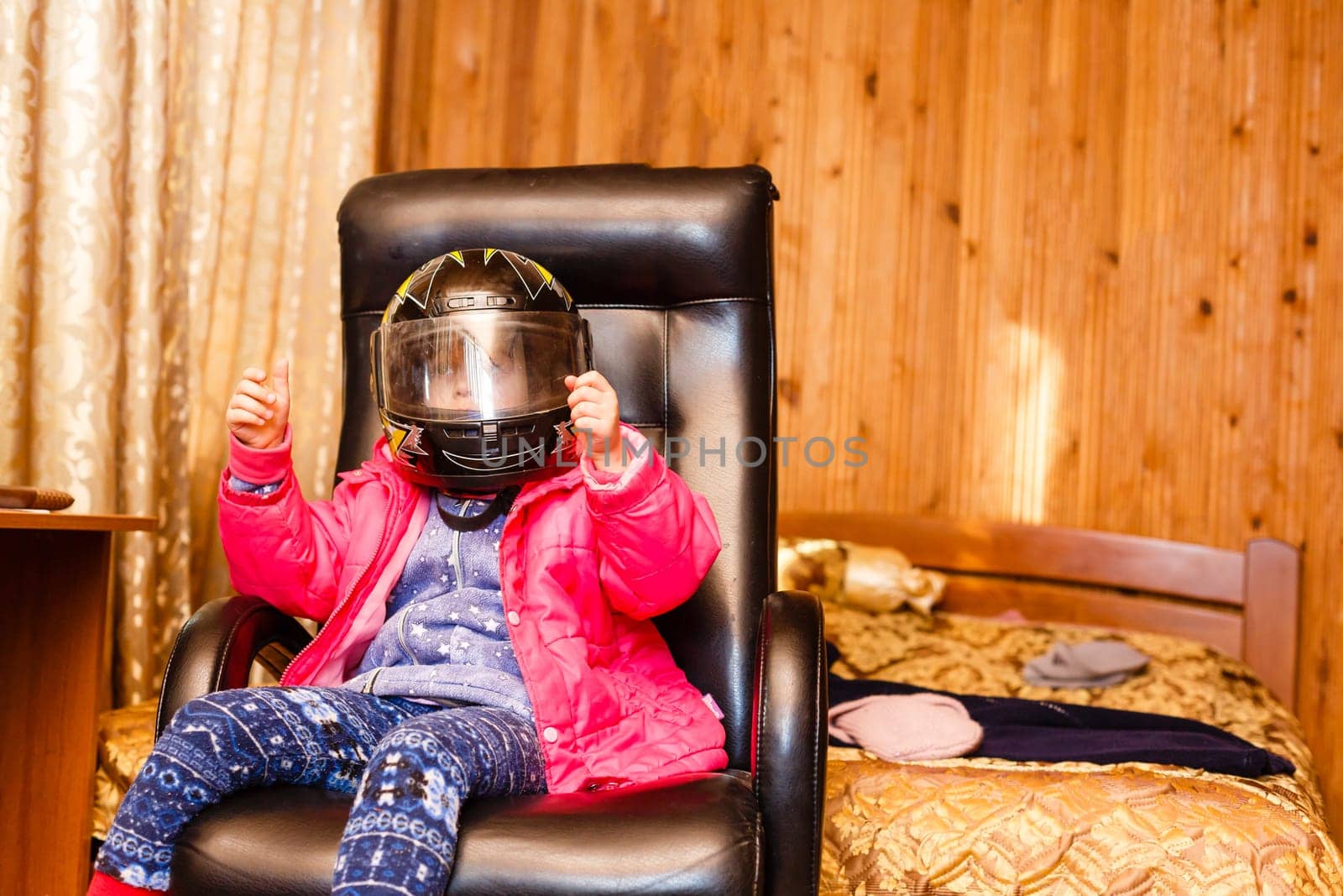 little girl in a motorcycle helmet in a chair at home by Andelov13